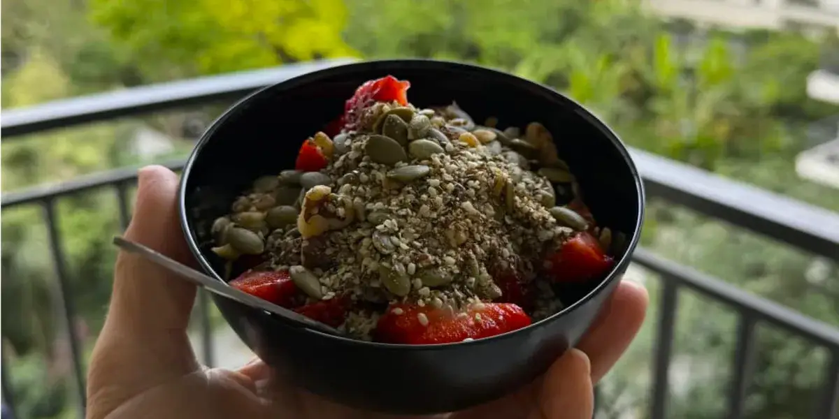 A yogurt bowl topped with seed and nut mix, berries, and honey